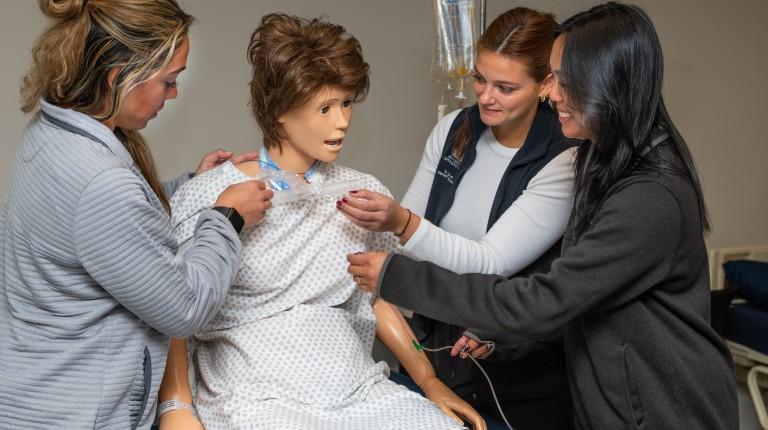 Three U N E students practicing on a patient simulator